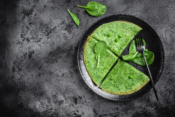 Green vegan crepes with spinach on dark background. Healthy breakfast, vegetarian food, banner, menu recipe place for text, top view