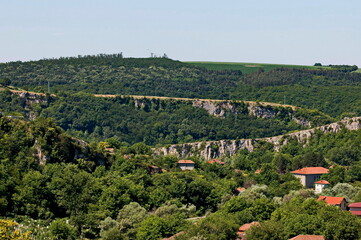 Fototapeta premium View of the beautiful village of Nisovo, Bulgaria, located below, above and in the high limestone cliffs, protected by magnificent deciduous trees