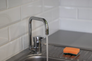 water tap in the kitchen with water jet and orange sponge