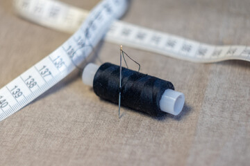 a spool of black thread with a needle and a centimeter on a linen fabric close-up