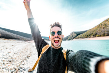 Happy man with backpack taking a selfie outdoors - Self portrait of a hiker smiling at camera -...