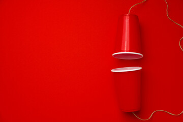 Red plastic cups connected with a thread on red background