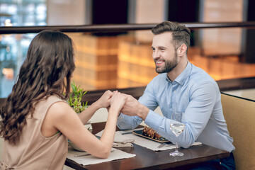 A couple sitting at the table in the restaurant and man holding womans hands