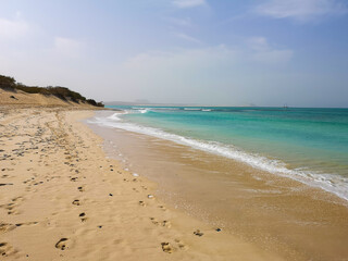 Footsteps on the sand and calm Atlantic Ocean water on the shore of Sal Rei, Cape Verde. African climate. Selective focus on the waves, blurred background.
