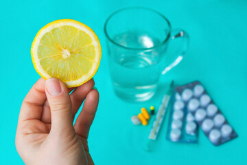 Lemon slice in female hand, medications on blue background, concept of preferring fruits to pills