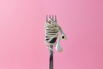 Headphones on a pink background. White headphones wrapped around a Fork. A portion of music