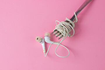 Headphones on a pink background. White headphones wrapped around a Fork. A portion of music