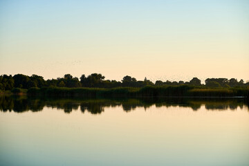 Landscape of a rural river with blue sky and trees on the background during sunset