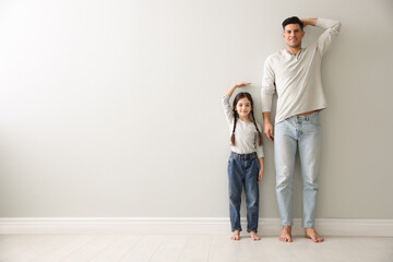 Little girl and father measuring their height near light grey wall indoors. Space for text
