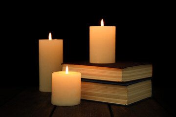 Burning candles and stack of books on wooden table in darkness