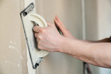 Worker sandpapers drywall joint. Closeup view