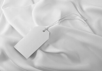 Plain white clothing tag label with hanging thread on white silky fabric