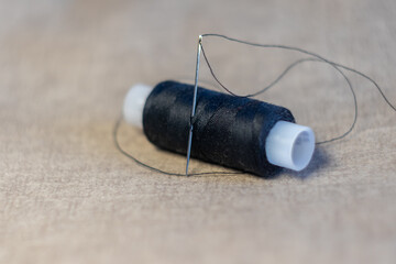 a spool of black thread with a needle on a gray background close up