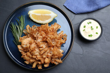 Delicious onion blossom served with lemon and sauce on black table, flat lay