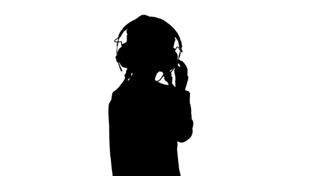 Silhouette Little girl dressed in white listening to the music in headphones and nodding her head to the rhythm.