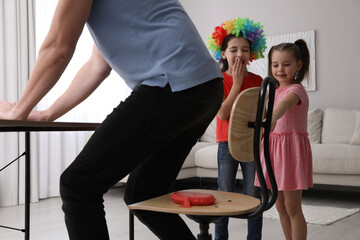 Cute little children putting whoopee cushion on father's chair while he sitting down at home,...