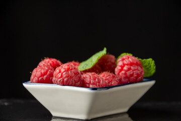 Close-up of raspberries and mint leaves in bowl, selective focus, on black slate, horizontal, with copy space