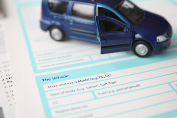 Blue toy car standing on insurance document closeup