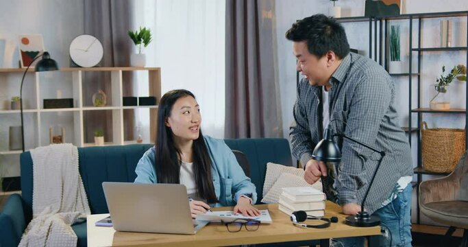 Likable positive friendly asian father and daughter being in contemporary home office working with her university's homework and after successfully ending task giving high five each other