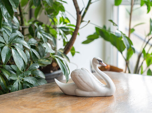 Graceful swan porcelain figurine -  on a wooden table with plants before the window