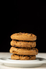 Fototapeta na wymiar Close-up of stack of chocolate cookies on plate, on white wooden table, black background, in vertical, with copy space