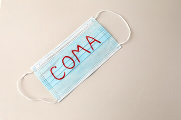 Medical mask with word Coma on beige background, top view