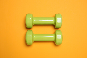 Dumbbells on orange background, flat lay. Sport equipment