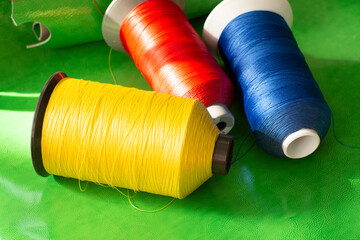 a spool of colorful threads on a green leather. Sewing thread. Shoe industry