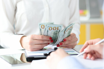 Business woman sitting at table with colleagues and counting money closeup