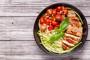 Fried chicken fillet and fresh vegetable salad of tomatoes, zucchini and pine nuts.