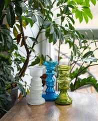 Mid-century modern artisan glass vase collection on a wooden table with plants before the window