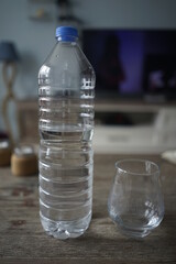Water and glass cup in a plastic bottle on a wooden background
