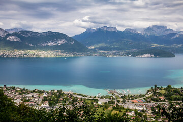 View of the Annecy lake surrounded of mountains  with cityscape in cloudy weather. Rhone Alps, France.