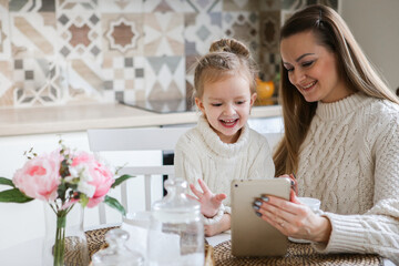Obraz na płótnie Canvas Smiling mother takes selfie with cute daughter on tablet, happy young mom laughing makes photo with daughter at home, single mom and adopted children playing fun with phone
