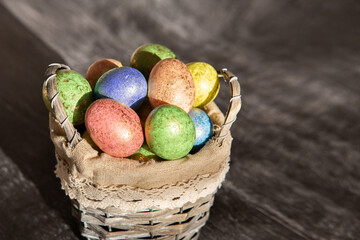 Easter colored eggs in a basket on dark wooden background.