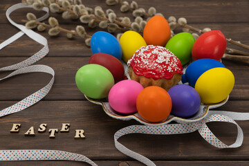 Fototapeta na wymiar colorful Easter eggs and pussy willow on vintage planks. painted in bright paint chicken eggs and cake in a plate on a wooden background. kulich, easter bread. lettering in wooden letters easter