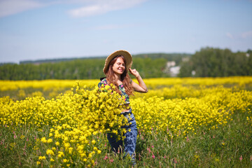 Naklejka na ściany i meble Young, beautiful woman in rapeseed field in the summer. Rural scene with attractive girl in hat enjoying sun in yellow blooming field. Concept of joy, happiness and freedom.