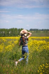 Young, beautiful woman in rapeseed field in the summer. Rural scene with attractive girl in hat enjoying sun in yellow blooming field. Concept of joy, happiness and freedom.