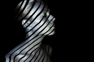 Portrait of a young lady with creative makeup. Conceptual idea of bold body art painting isolated on black background. Abstract picture of diagonal lines on woman face.