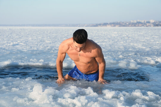 Man getting out of ice hole on winter day. Baptism ritual