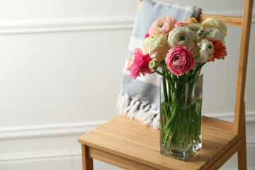 Beautiful ranunculus flowers in vase on wooden chair indoors, space for text