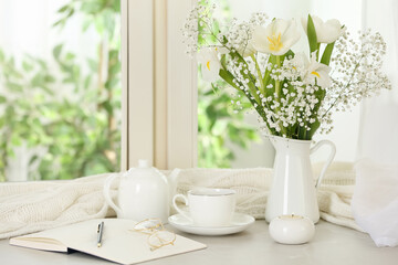 Fototapeta na wymiar Beautiful fresh flowers, hot coffee and notebook on window sill indoors