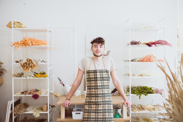 Junger Mann in Gärtnerschürze vor Trockenblumen