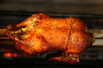 Grilling whole delicious duck in rotisserie machine, closeup