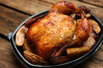 Delicious grilled whole chicken with potato in plastic container on wooden table, closeup. Food delivery service