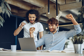Two excited overjoyed young businessmen looking at laptop screen happy to win or recieved good news