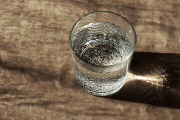 sparkling water glass and sunlight shadows on beige background. copy space. minimal food concept