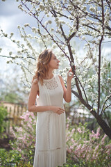 Naklejka premium beautiful girl in a white dress walks in the garden, sakura blooming, spring bloom