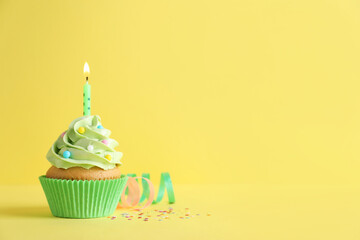 Delicious birthday cupcake with burning candle, sprinkles and streamers on yellow background, space for text