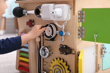 Little boy playing with busy board house indoors, closeup